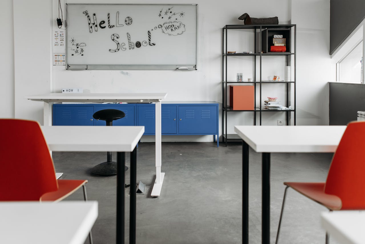 Empty chairs and desks of a classroom; and a white board for writing.