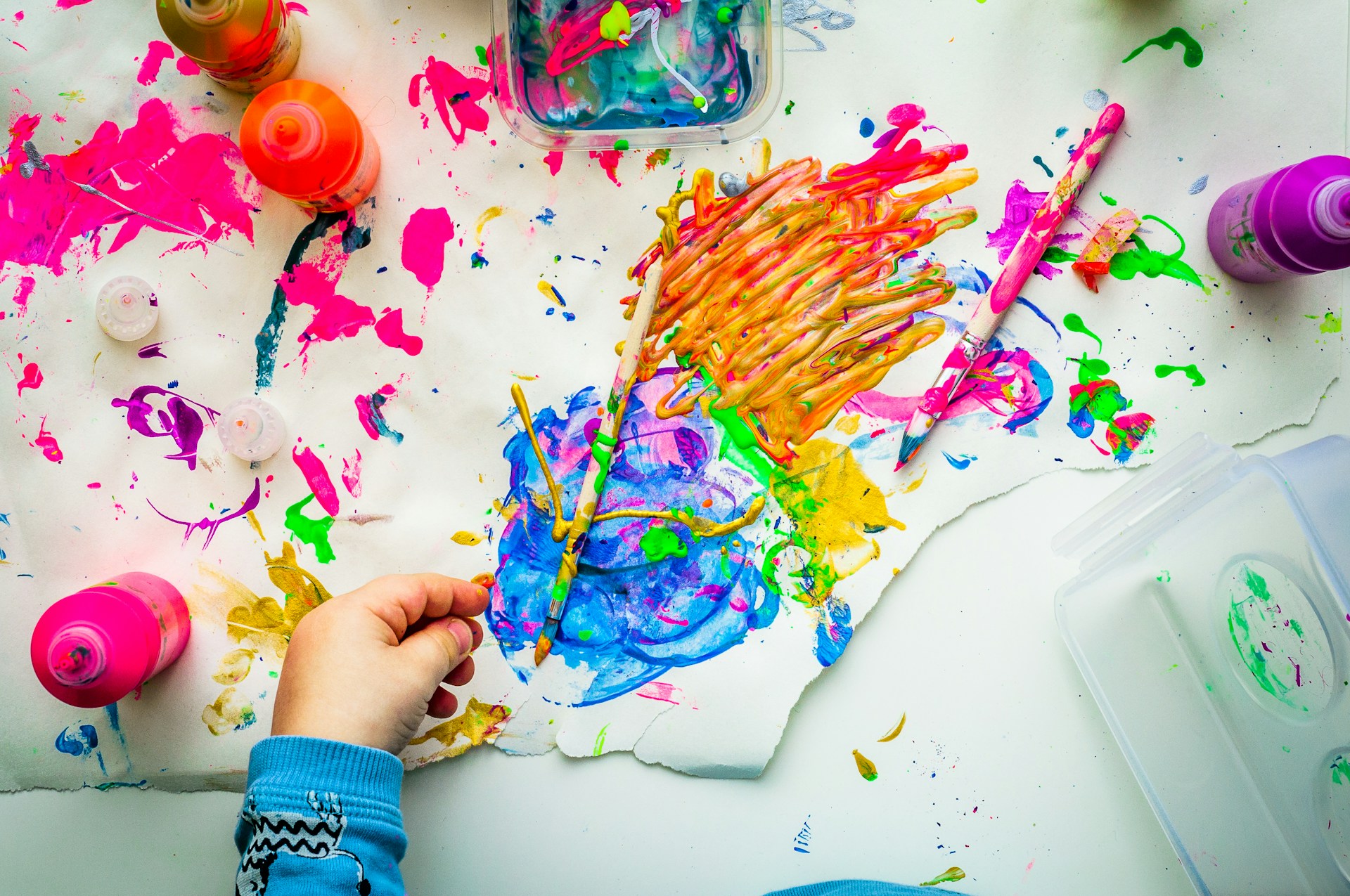 Splash of different colors on canvas with a child's hand over it.