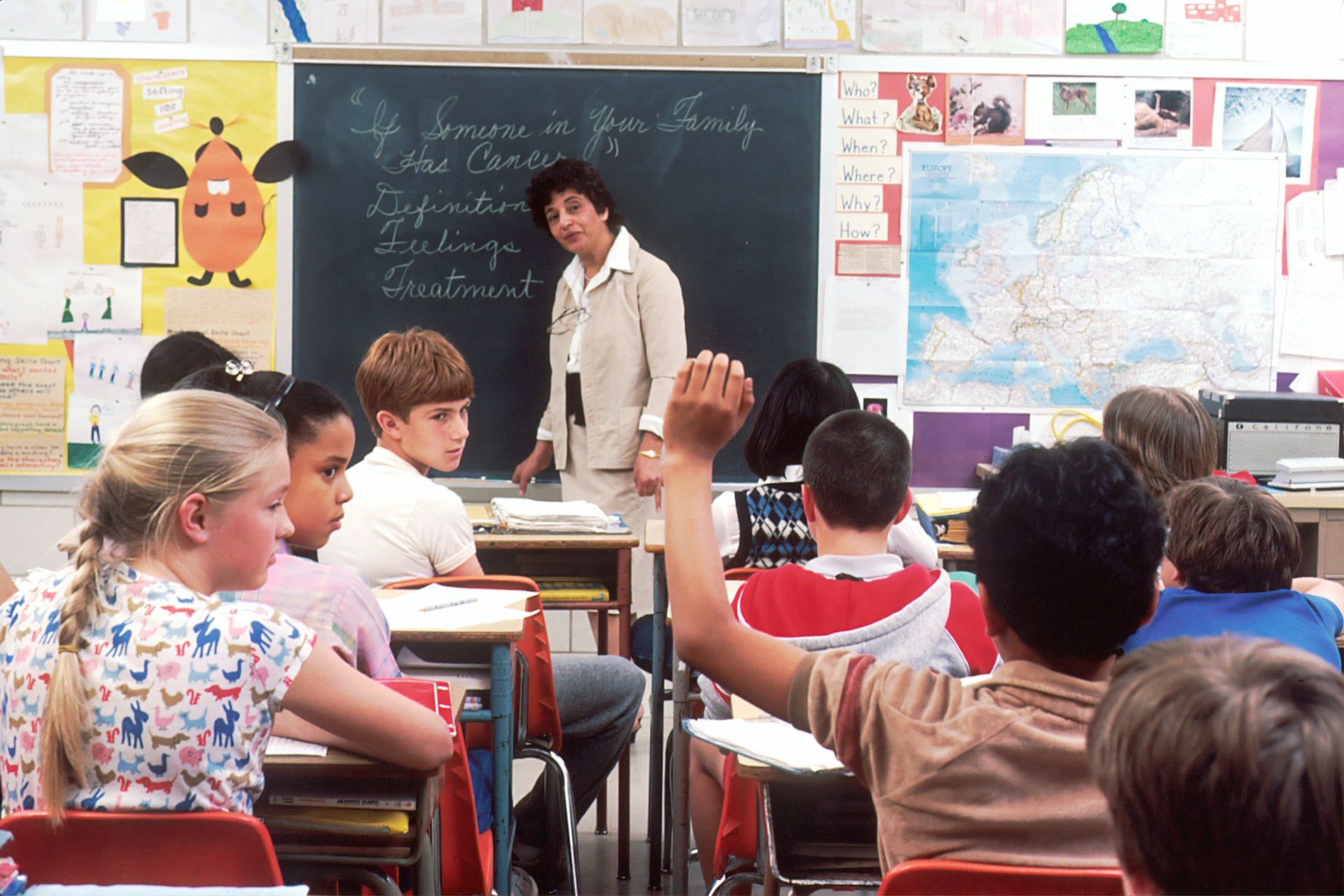 Teacher standing before a blackboard and students in a classroom.