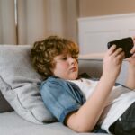 A teen boy watching mobile phone laying on his bed.