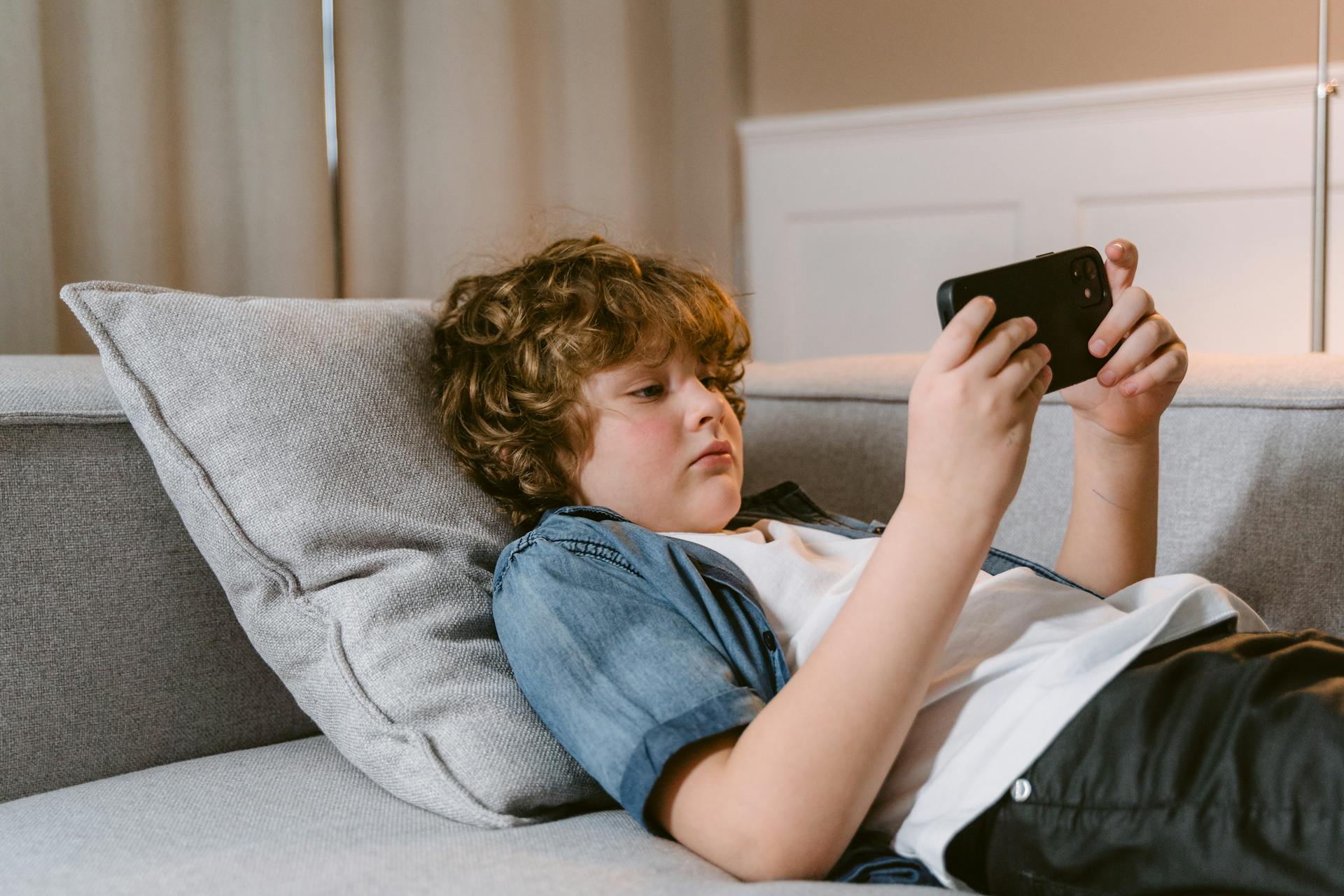 A teen boy watching mobile phone laying on his bed.