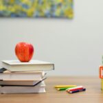 Books, an apple, crayons, and A B C alphabets on a table in classroom.