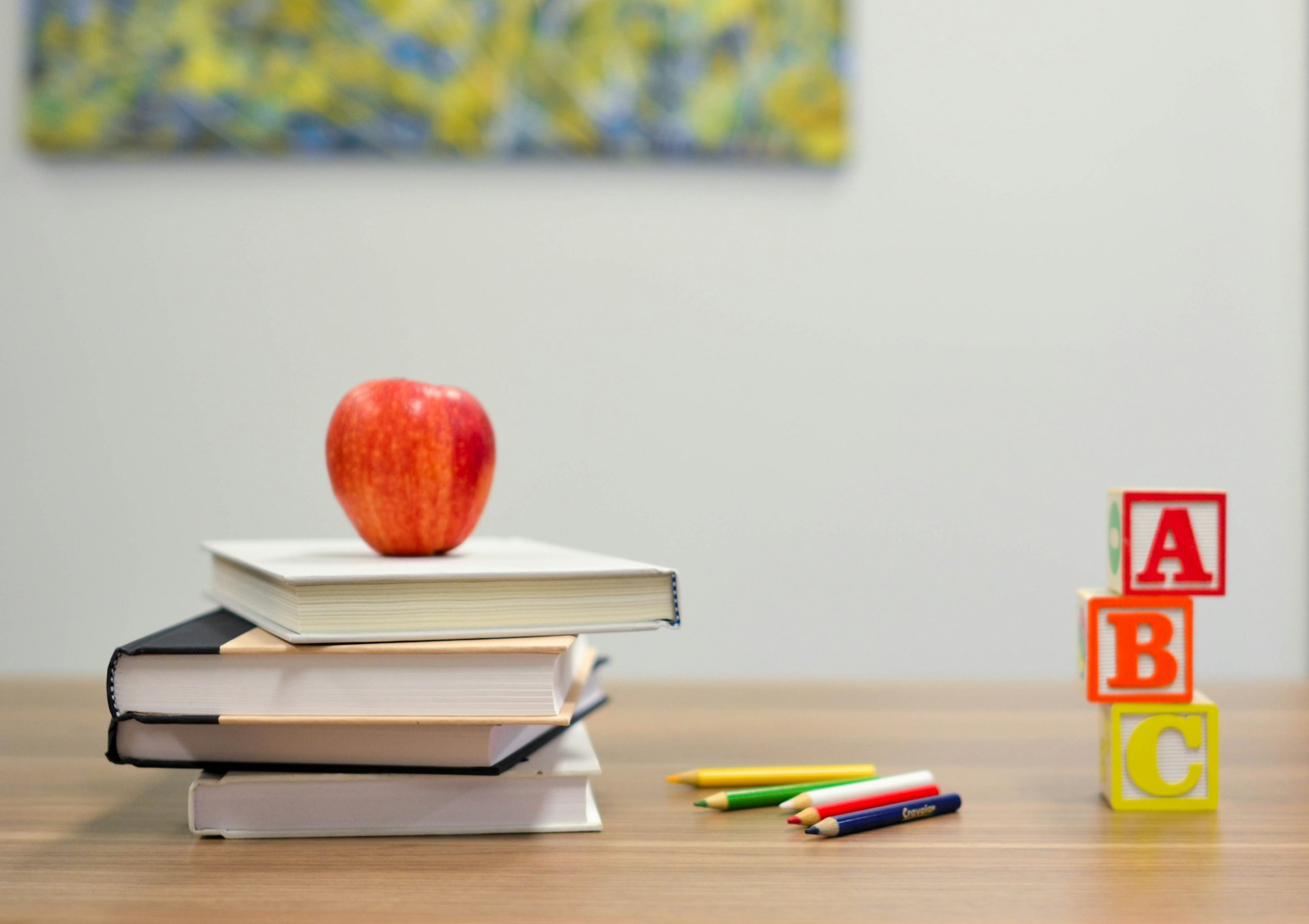 Books, an apple, crayons, and A B C alphabets on a table in classroom.