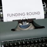 Typewriter with a paper in it typed 'funding round' text over it.