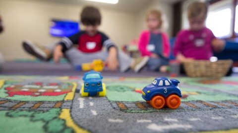 Kindergarten students playing on the floor with toy trucks.