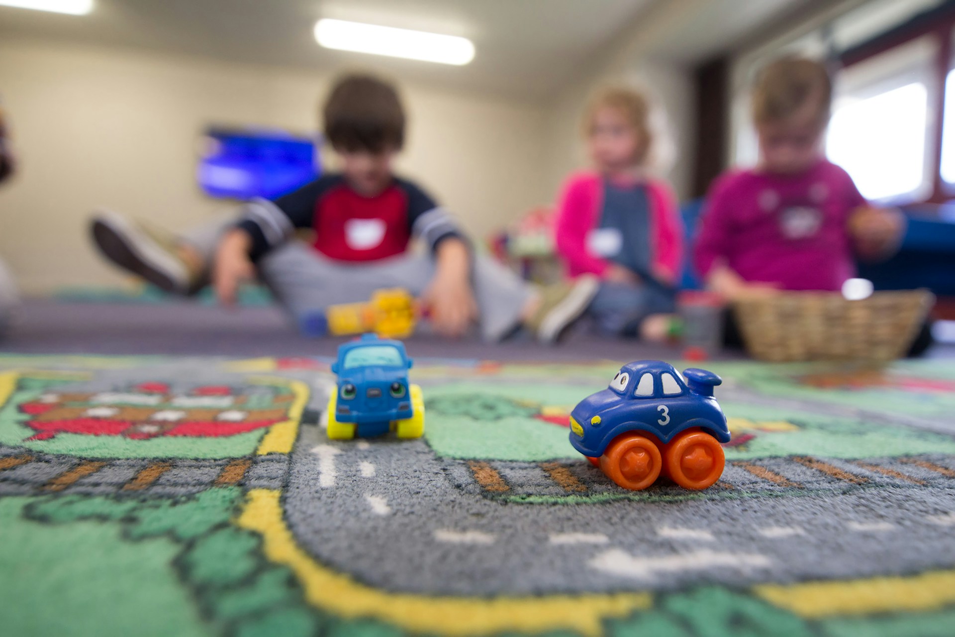 Kindergarten students playing on the floor with toy trucks.
